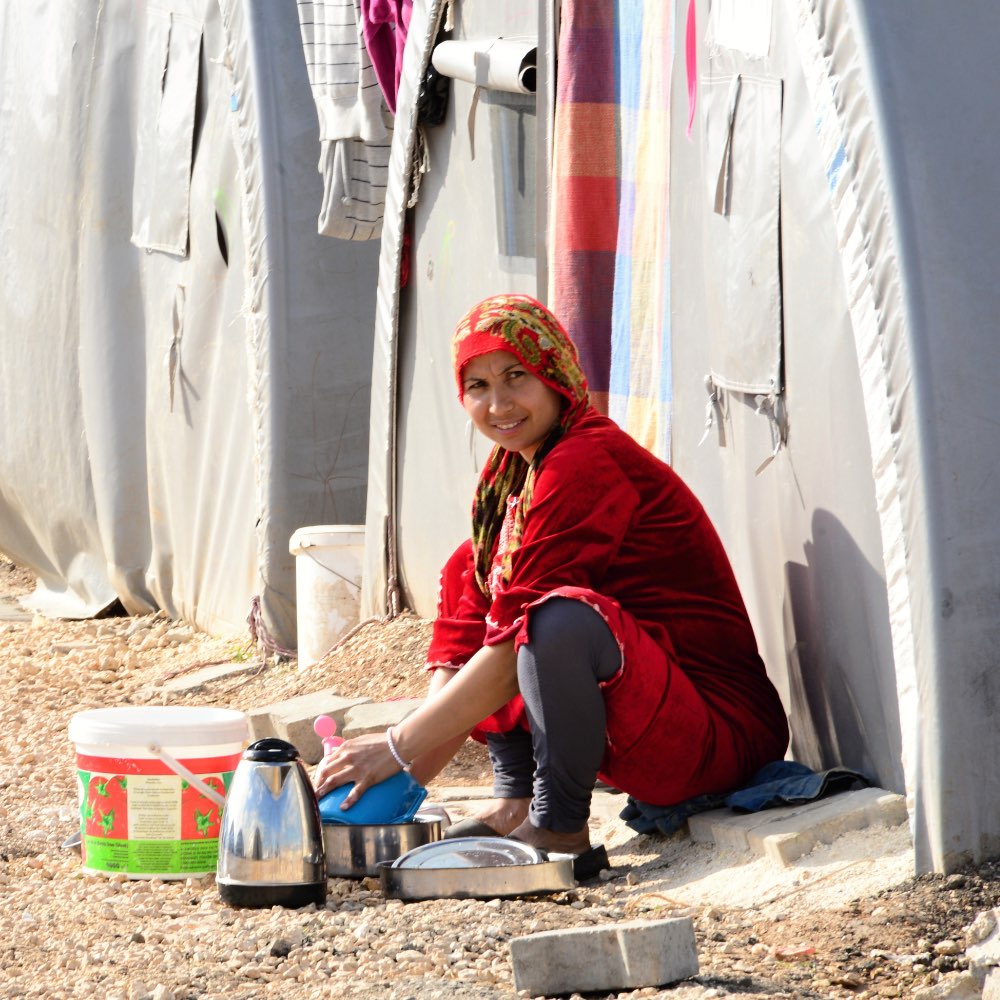 A woman in a refugee camp smiling outside her living quarters